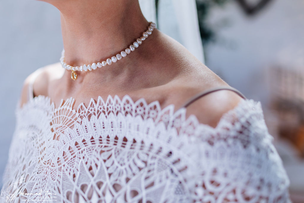 image of the neckline of a boho wedding dress with scalloped lace edges on a bardot cut neckline. The bride wears a sea inspired wedding necklace